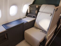 Business class seat with beige leather personal console and window view inside a modern airplane cabin