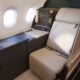 Business class seat with beige leather personal console and window view inside a modern airplane cabin
