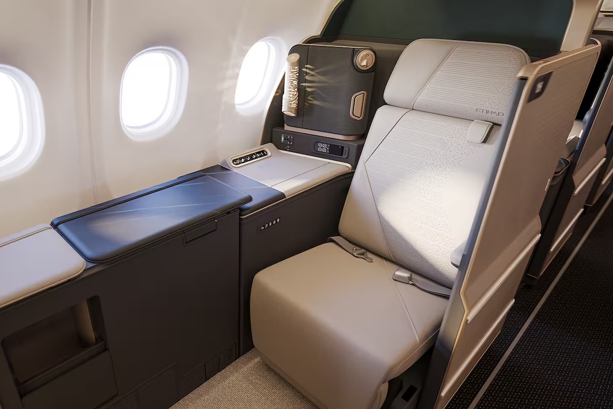 Business class seat with beige leather personal console and window view inside a modern airplane cabin