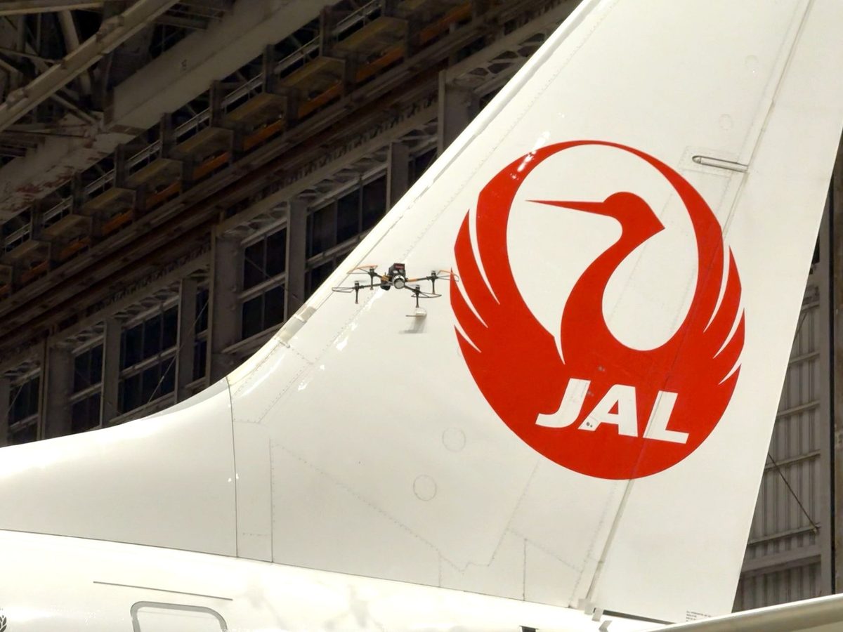 image Japan Airlines tail with red crane logo inside a maintenance hangar a small quadcopter drone sits on the fuselage surface