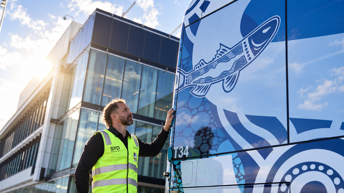 image Man in a neon safety vest touches a blue bus with a fish graphic beside a modern glass building at sunset