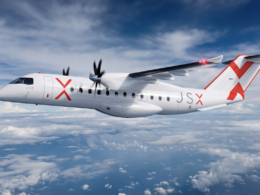 White twin turboprop regional jet in flight over a cloudy blue sky with red JSX branding on fuselage and tail
