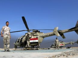 Iraqi Army helicopter on a desert airstrip with soldiers standing nearby under a blue sky