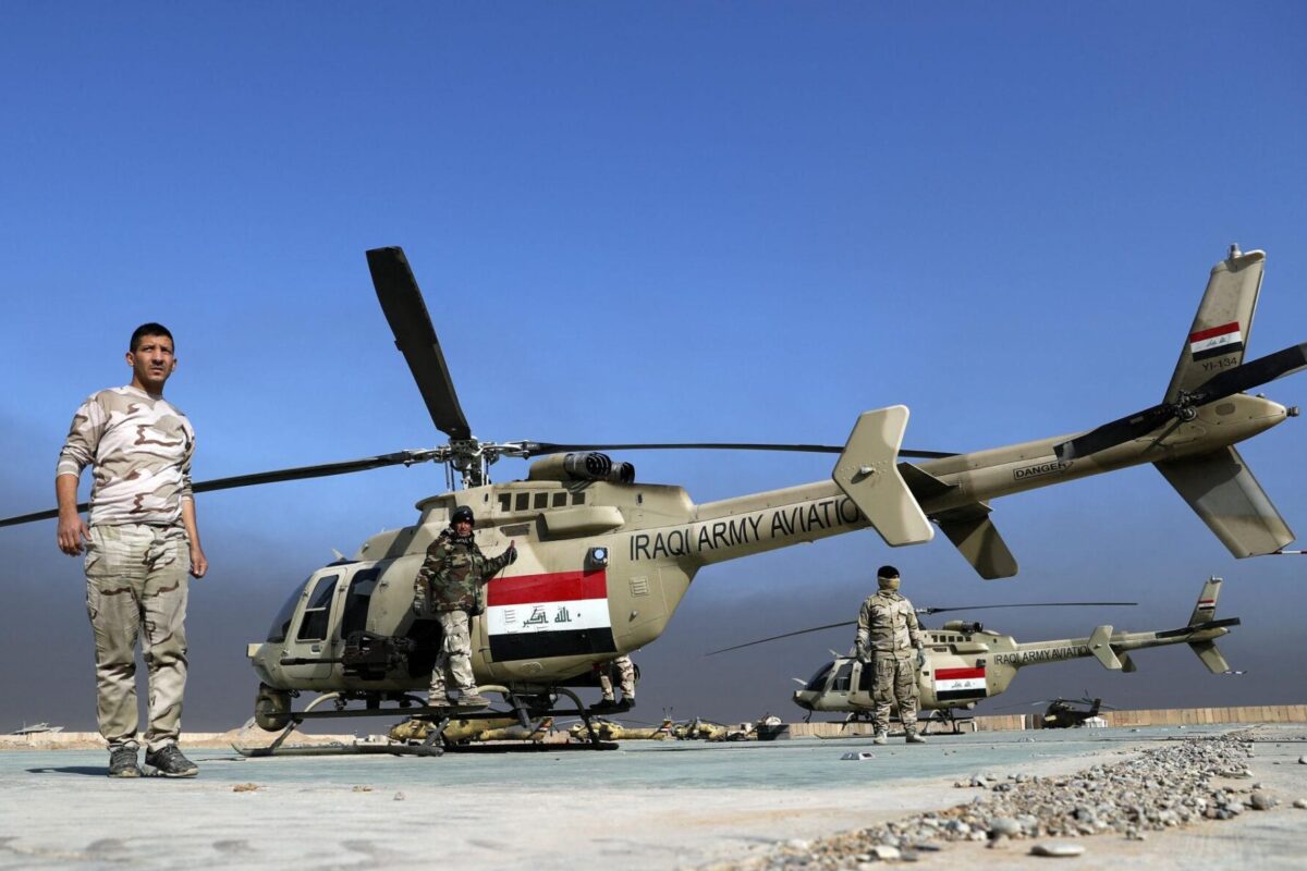 Iraqi Army helicopter on a desert airstrip with soldiers standing nearby under a blue sky