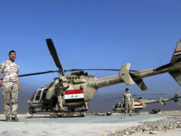 Iraqi Army helicopter on a desert airstrip with soldiers standing nearby under a blue sky