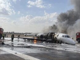 Aircraft wreck on runway with fire and smoke firefighters respond with hoses and fire trucks nearby