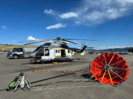 Rescuer helicopter on a tarmac with ground support gear and a red inflatable helicopter float near it under a blue sky