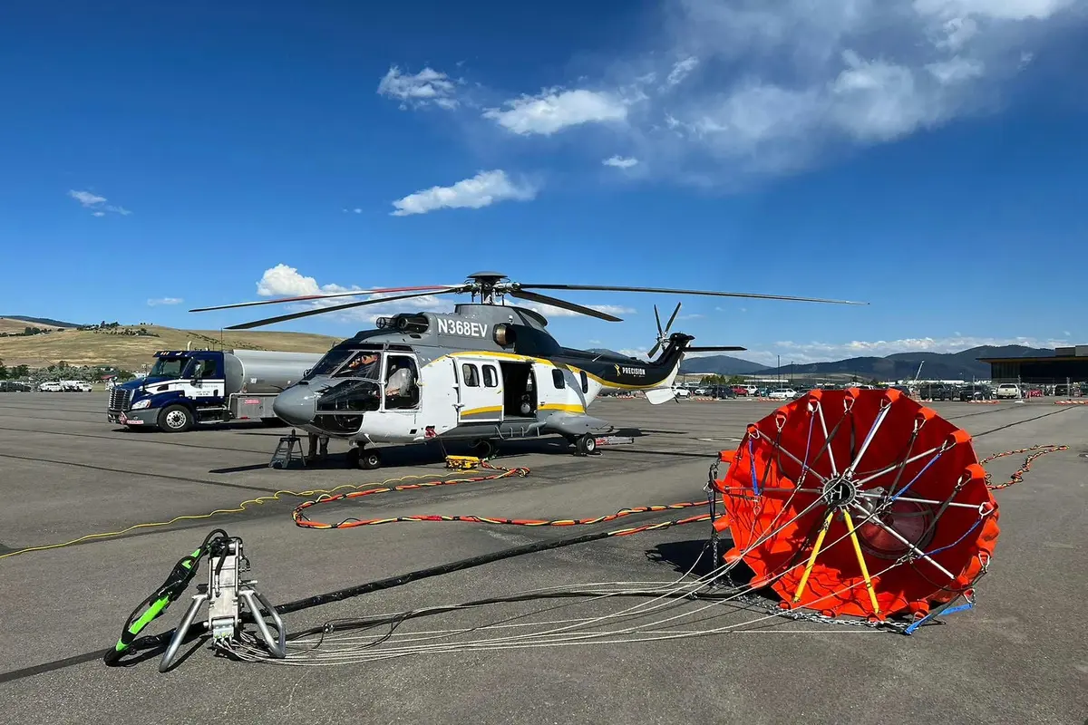 Rescuer helicopter on a tarmac with ground support gear and a red inflatable helicopter float near it under a blue sky