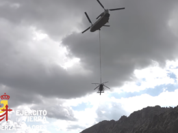 Military helicopter with long line lowering a suspended load over a rocky mountain landscape logo reading Ejército de Tierra in the corner