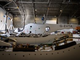 Maintenance hangar with a white aircraft fuselage labeled G EVTA undergoing assembly or repair surrounded by tools and equipment