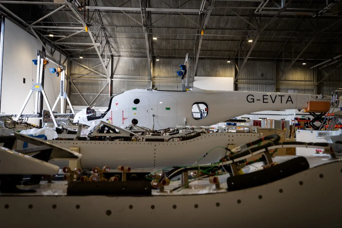 vertical aerospace assembly Maintenance hangar with a white aircraft fuselage labeled G EVTA undergoing assembly or repair surrounded by tools and equipment