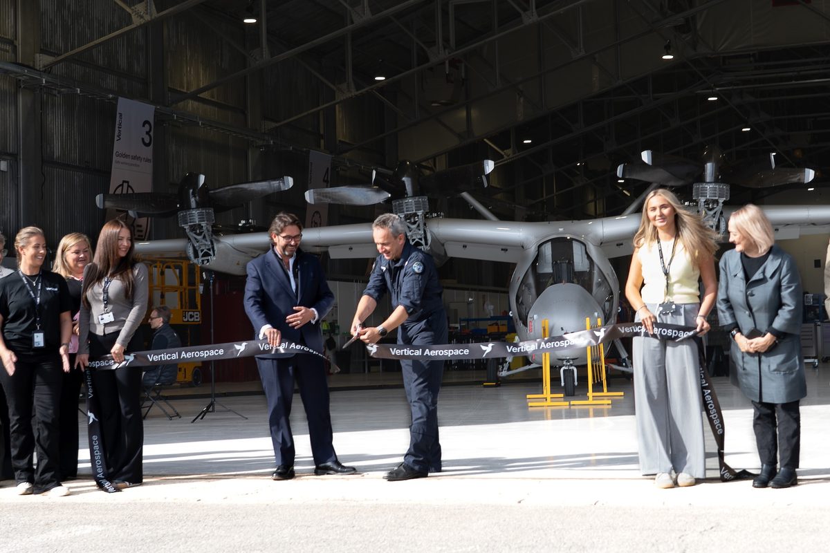 vertical aerospace factory opening Group of professionals and staff at a Vertical Aerospace ribbon cutting ceremony beside a helicopter in a hangar celebrating