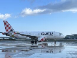 Volotea airplane on a wet runway with a colorful patterned tail blue sky above and clouds nearby