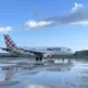 Volotea airplane on a wet runway with a colorful patterned tail blue sky above and clouds nearby