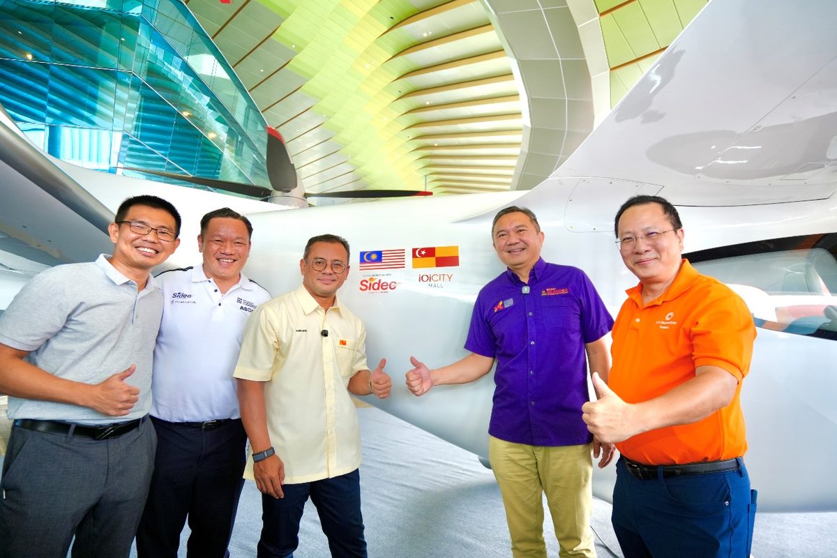 05 TCab SIDEC Group Photo Five men stand beside a white aircraft giving thumbs up in a bright hangar with national flags on the fuselage Malaysia Singapore Spain