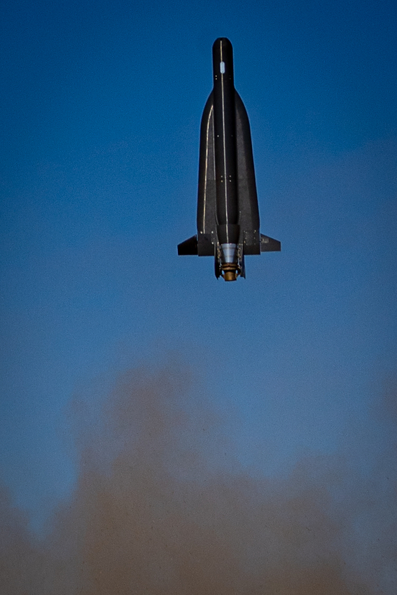 A Cummings Aerospace Hellhound S3 turbojet powered loitering munition in flight Rocket blasting off vertically into a blue sky with a brown smoke plume at launch