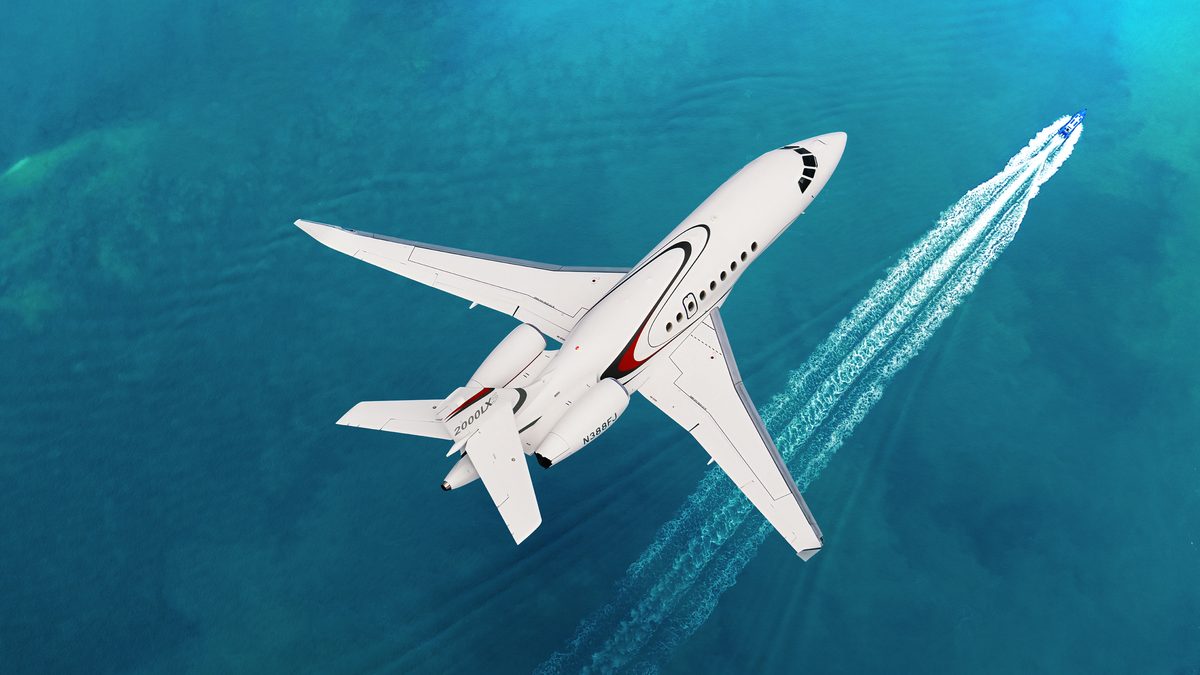 A Dassault Falcon 2000LXS in flight White private jet flying over blue ocean leaving a white wake behind it