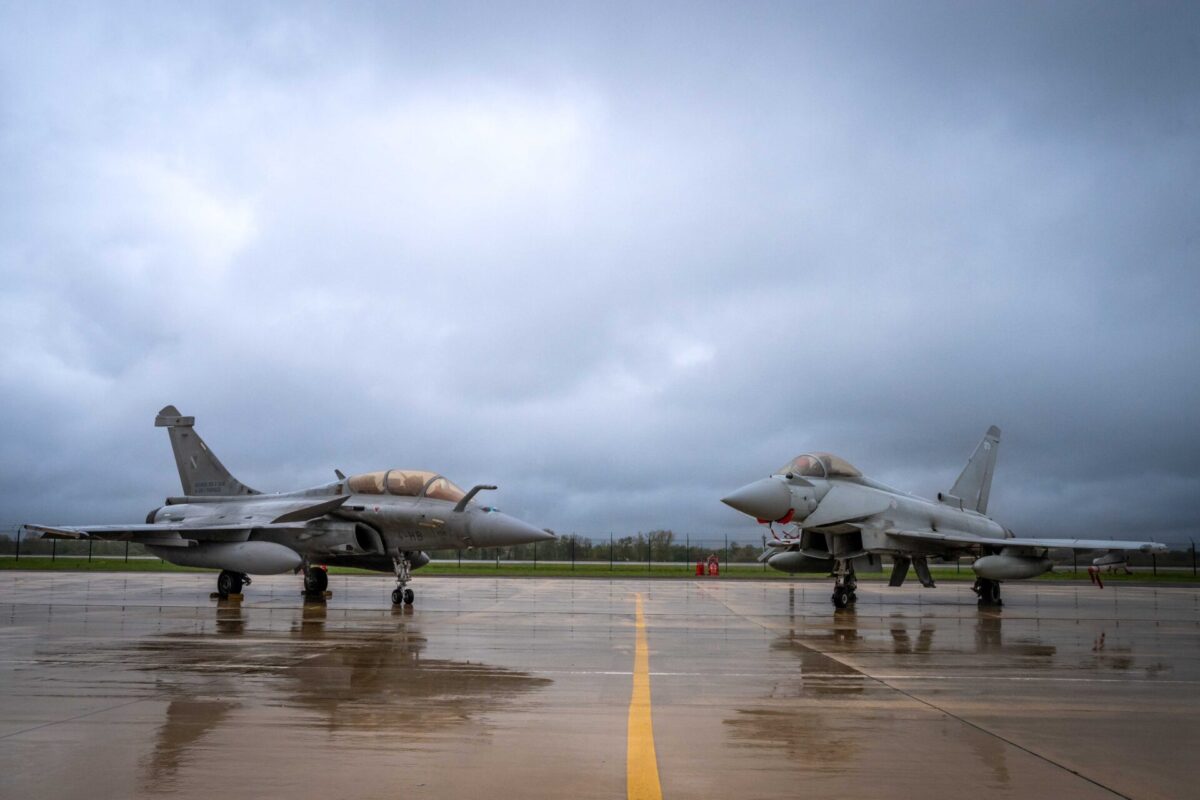 A French Air and Space Force Rafale B and a Royal Air Force Eurofighter Typhoon Two fighter jets lined up on a wet tarmac under a cloudy sky with a yellow line marking the center