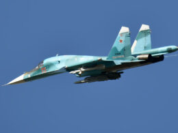 Russian fighter jet in teal livery with red star insignia and the number 15 flying against a clear blue sky