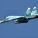 Russian fighter jet in teal livery with red star insignia and the number 15 flying against a clear blue sky