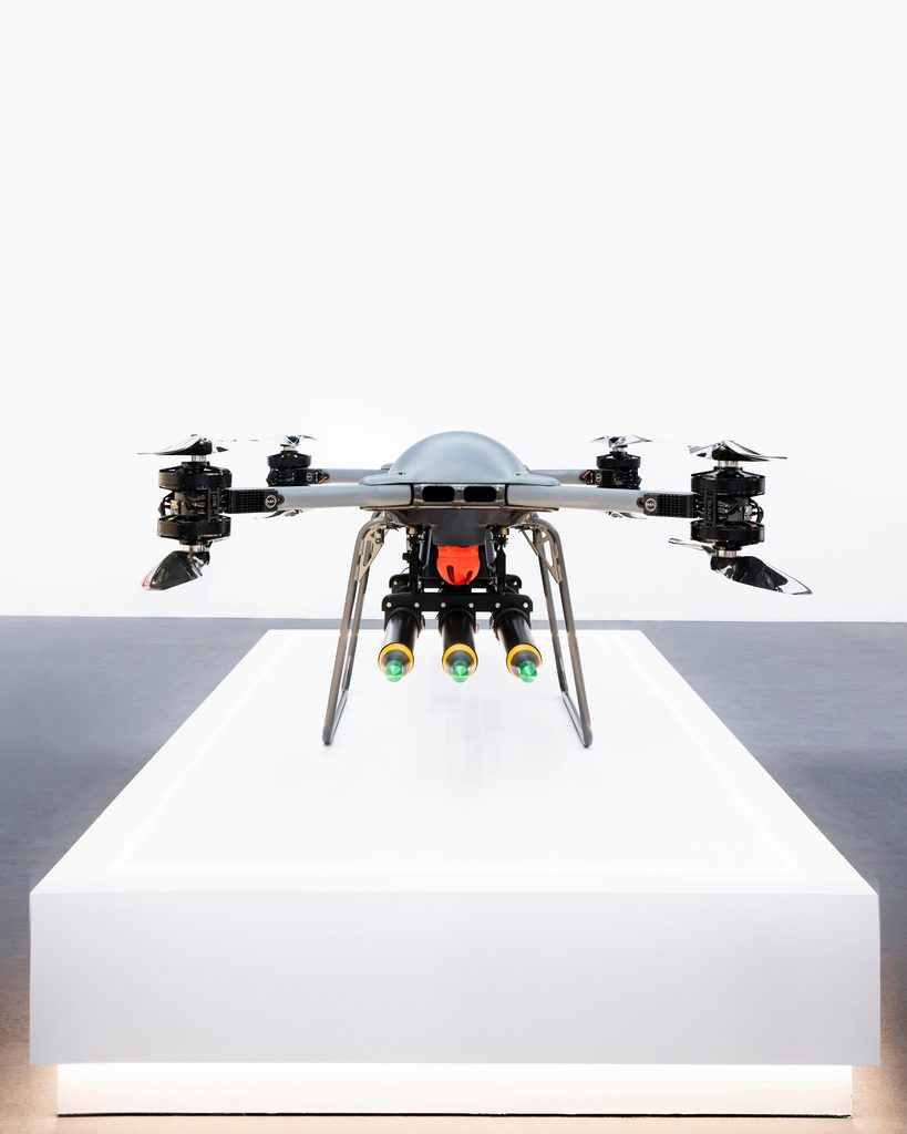 A TRV 150 uncrewed aircraft fitted with a three round launcher Front view of a professional quadcopter drone mounted on a white pedestal in a bright studio display