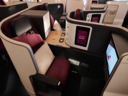 Private business class airplane cabin with individual suites burgundy seats high back headrests personal touch screen screens and wooden tray tables
