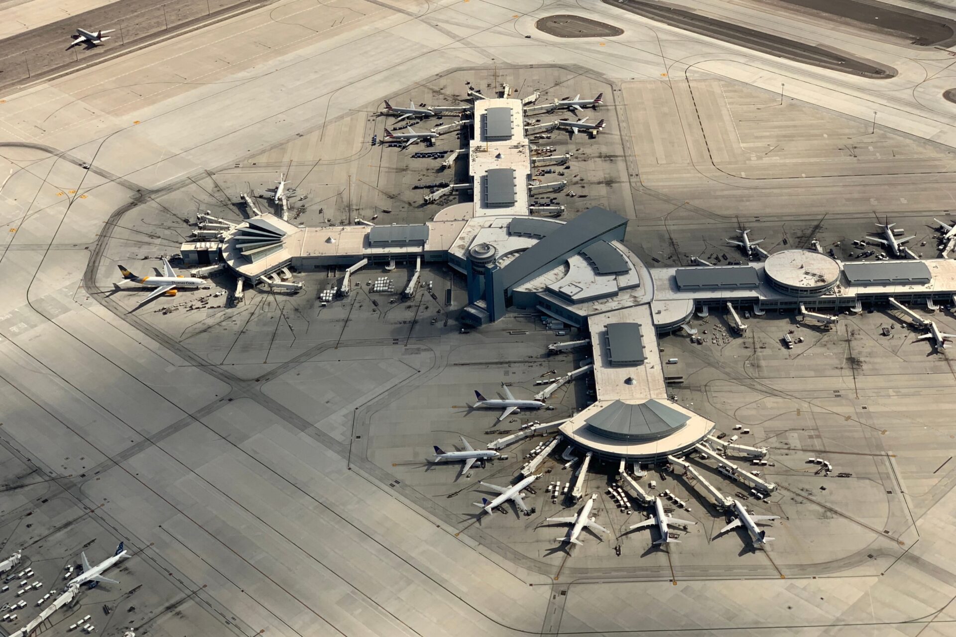 Aircrafts in the Tarmac Aerial view of a large airport terminal with many jet bridges and airplanes docked at gates around a central concourse