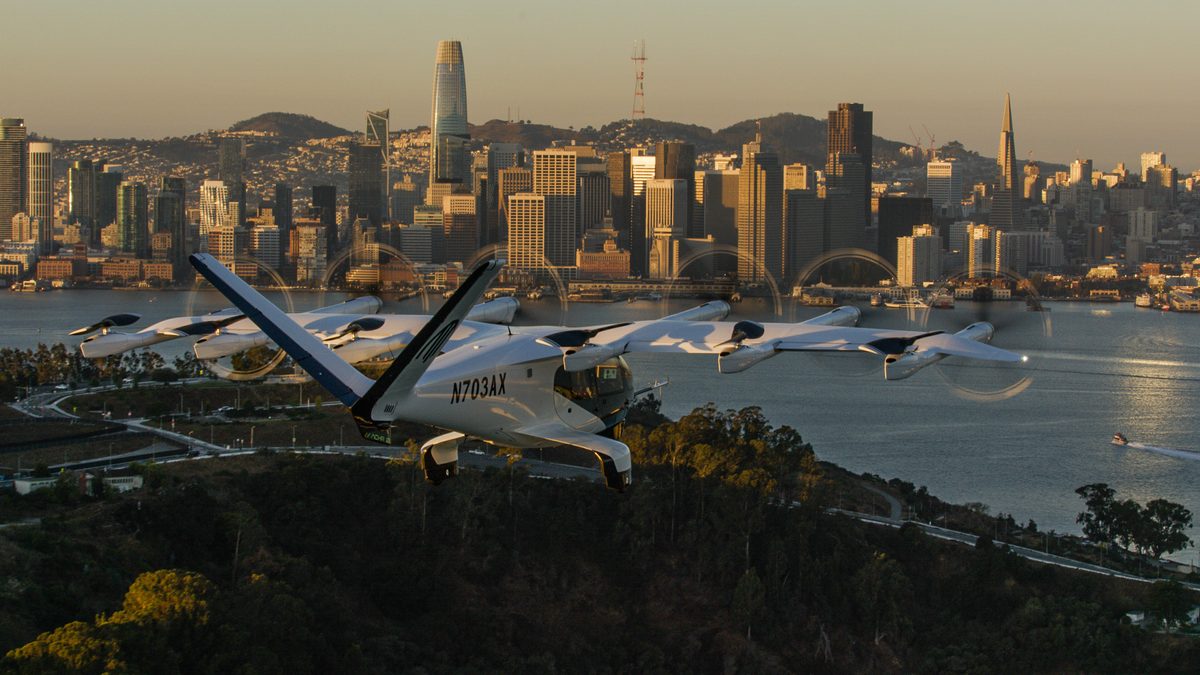 Archer Bay Area No Roads Tour Still 01 Seaplane with registration N703AX over a bay and a city skyline at sunset aircraft in foreground