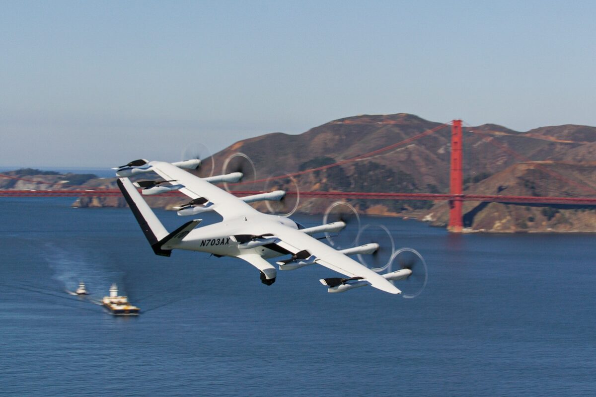 Archer Bay Area No Roads Tour Still 02 White tilt rotor aircraft flying low over the bay with a red suspension bridge and hills in the background