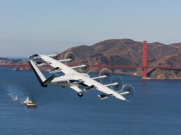 White tilt rotor aircraft flying low over the bay with a red suspension bridge and hills in the background