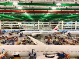 Inside a spacious aircraft maintenance hangar with a Japan Airlines plane and green and red overhead beams above the tarmac area