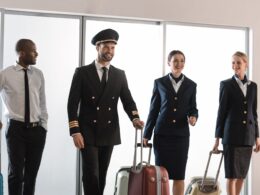 Group of airline crew in uniform standing with rolling suitcases in a bright airport setting