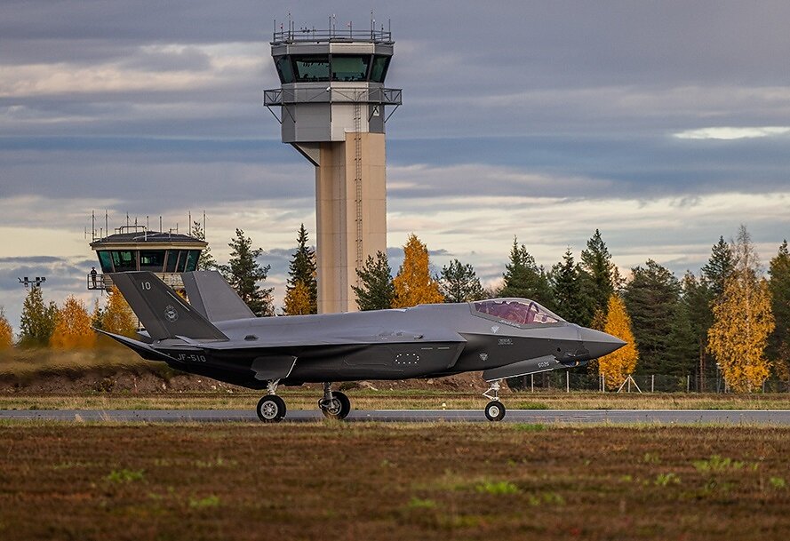 Finnish Air Force F 35A JF 510 at Rovaniemi Airport in Finland 2 Gray stealth fighter jet on a runway with a control tower and autumn trees in the background cockpit canopy tinted pink