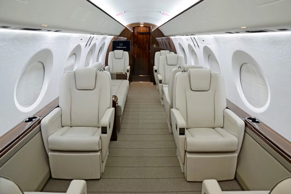 Recently Saved 1 of 1 1 Interior of a private jet cabin with beige leather seats forming two rows along a central aisle and wooden accents by the windows empty and luxurious