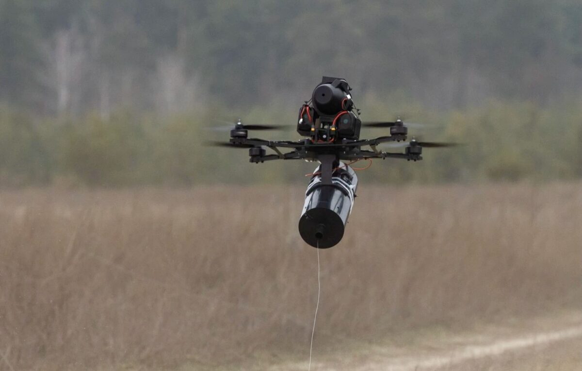 Recently Saved 1 of 1 10 Quadcopter drone with a cylindrical payload hanging from a tether over a grassy field