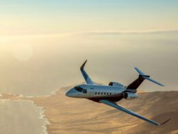 Private jet flying over a sunlit desert coastline at sunset viewed from the side