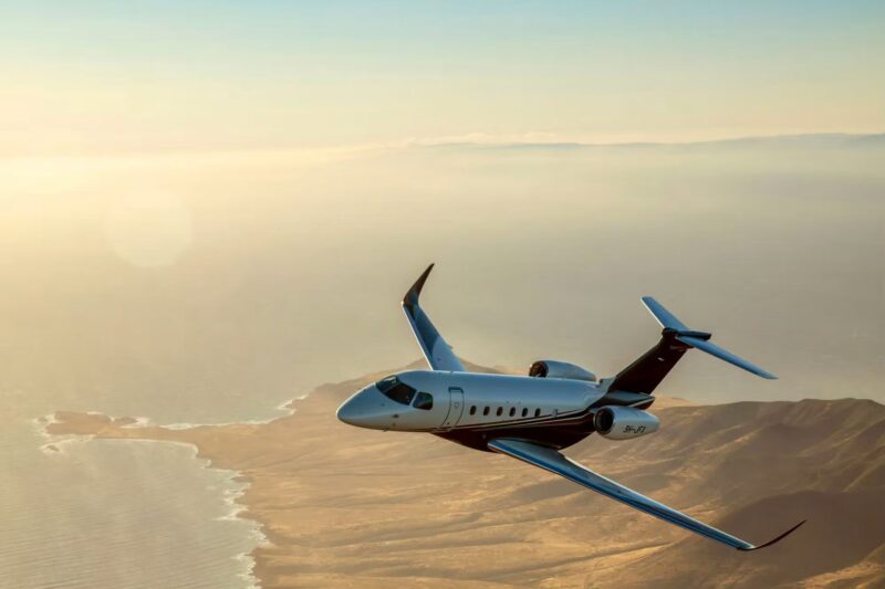 Private jet flying over a sunlit desert coastline at sunset viewed from the side