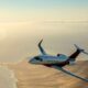Private jet flying over a sunlit desert coastline at sunset viewed from the side