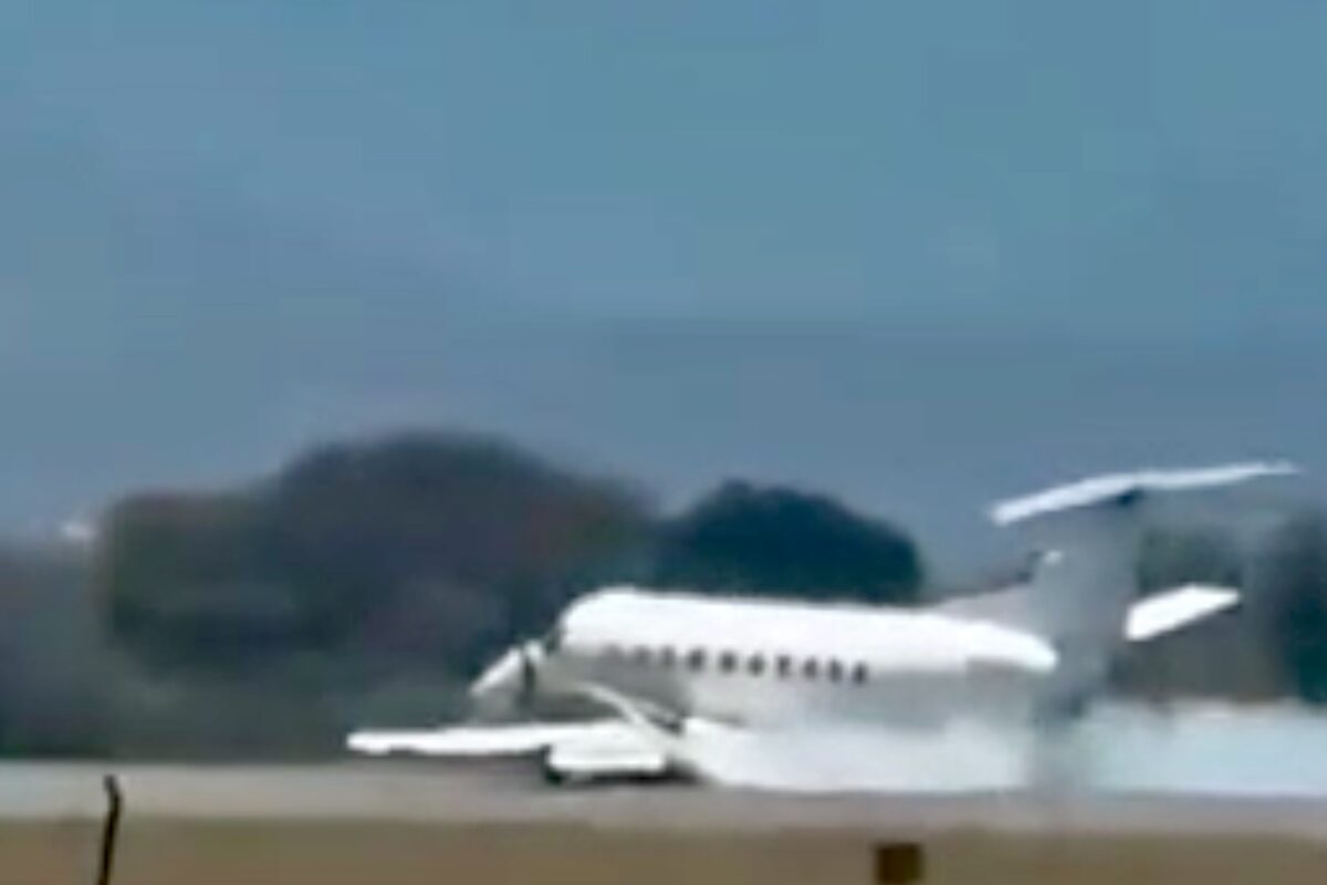 Small white jet parked on a runway with trees and a blue sky in the background