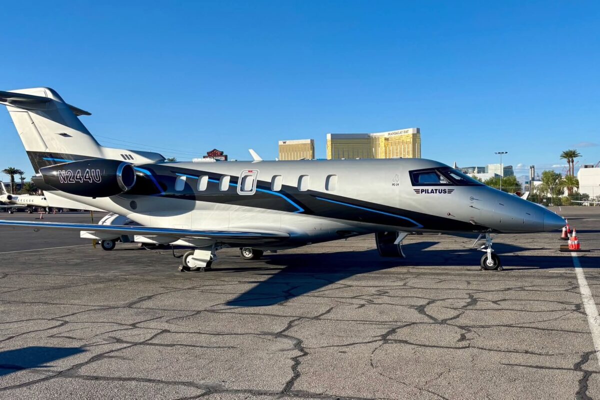 Side view of a Pilatus PC 24 private jet parked on a tarmac gray and black with blue accents tail number N244U