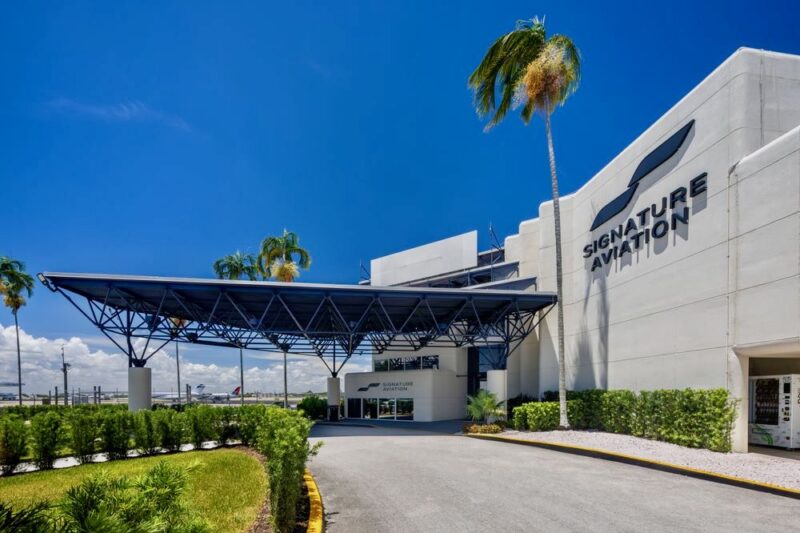 Signature Aviation building with a large blue canopy over the entrance and palm trees under a sunny blue sky