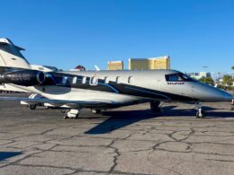 Side view of a Pilatus PC 24 private jet parked on a tarmac gray and black with blue accents tail number N244U