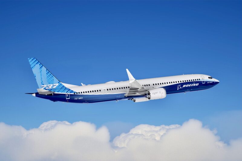 Recently Saved 1 of 1 14 Blue and white Boeing 737 MAX airliner flying high above fluffy clouds against a clear blue sky