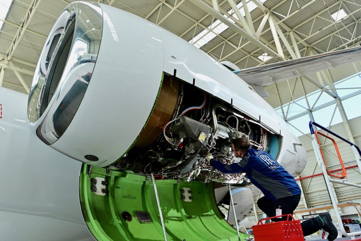 Aircraft engine maintenance a technician in a blue uniform works inside an open jet engine nacelle in a hangar with exposed wiring and components visible