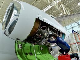 Aircraft engine maintenance a technician in a blue uniform works inside an open jet engine nacelle in a hangar with exposed wiring and components visible