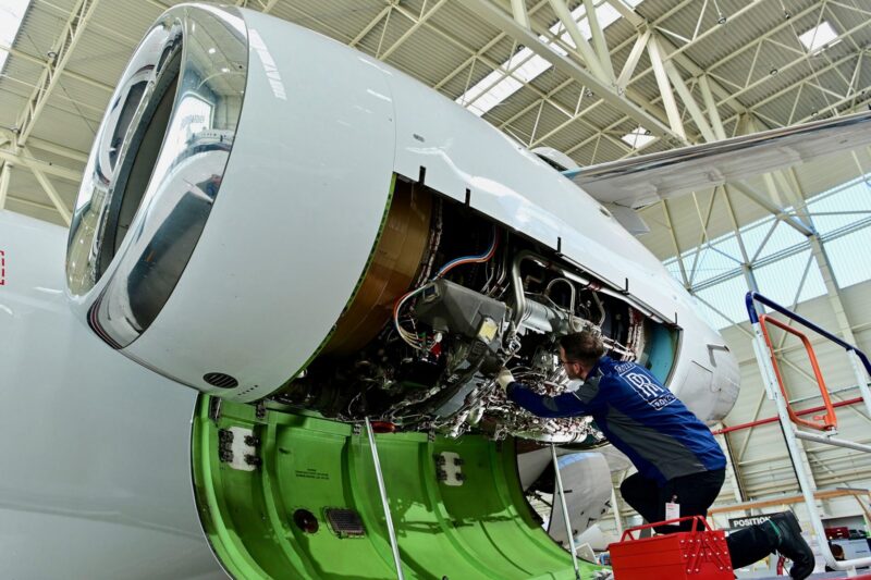 Aircraft engine maintenance a technician in a blue uniform works inside an open jet engine nacelle in a hangar with exposed wiring and components visible