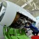 Aircraft engine maintenance a technician in a blue uniform works inside an open jet engine nacelle in a hangar with exposed wiring and components visible