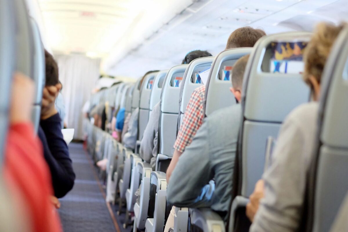 Recently Saved 1 of 1 17 Passengers seated in rows inside a commercial airplane cabin viewed from the aisle with overhead bins above