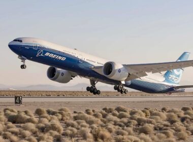 Boeing passenger jet lifting off from a desert runway with shrubs in the foreground.