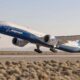Boeing passenger jet lifting off from a desert runway with shrubs in the foreground